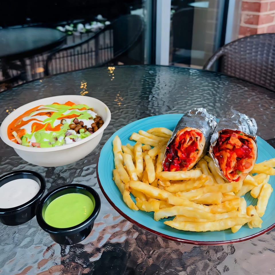 Indian wraps with fries, a colorful bowl, and dipping sauces on a glass table.
