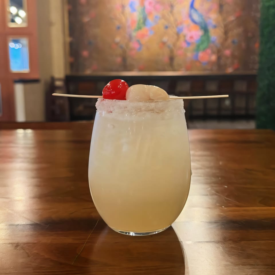 A lychee martini with a sugared rim, garnished with a cherry and lychee, on a wooden table.